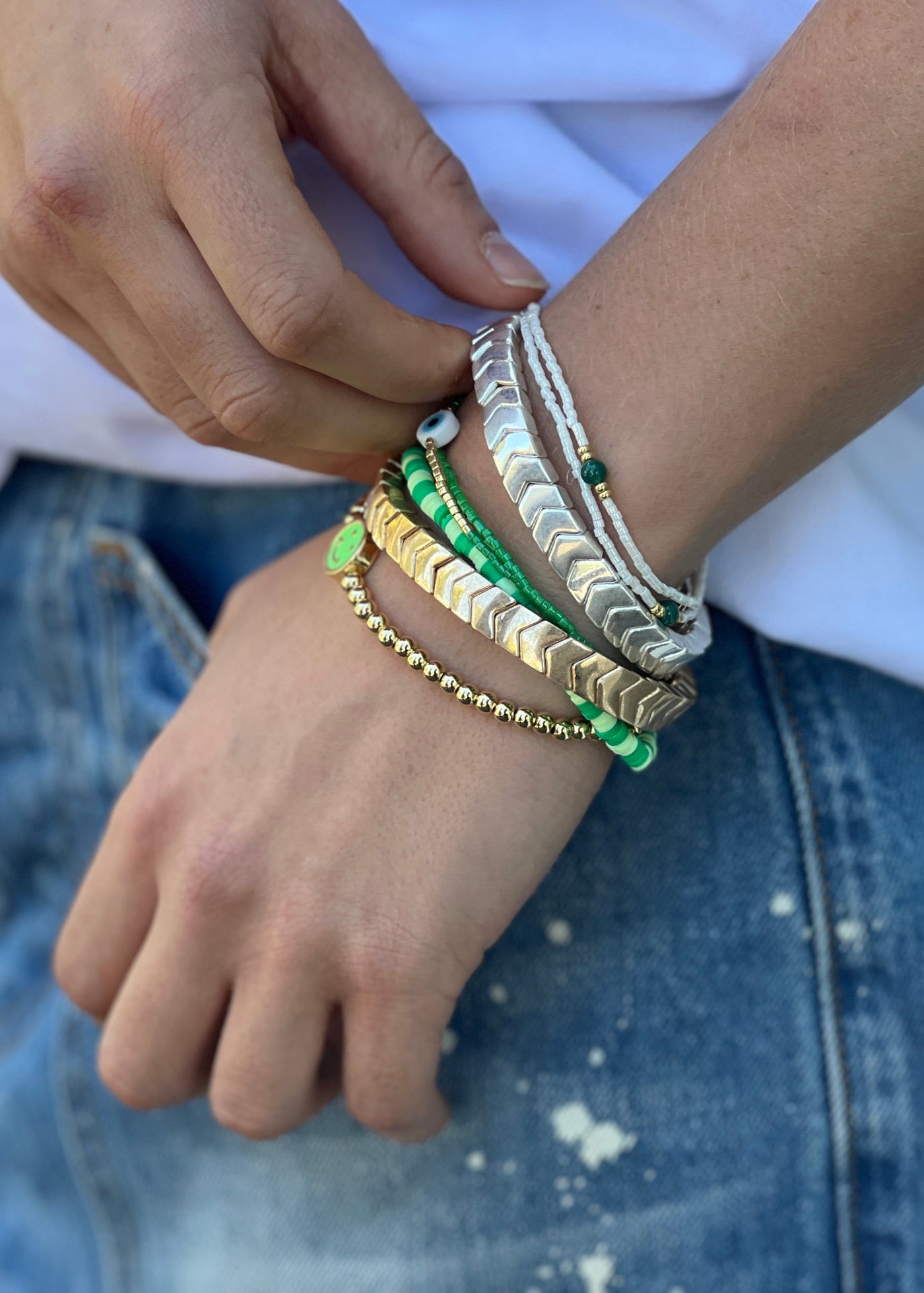 Hammill & Co Colourful set of 8 bracelets on elastic. Features gold and silver bracelets,  mixed fine beaded bracelets in green and white and feature gold bracelet with green smily fave.

