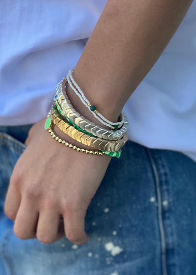 Hammill & Co Colourful set of 8 bracelets on elastic. Features gold and silver bracelets,  mixed fine beaded bracelets in green and white and feature gold bracelet with green smily fave.

