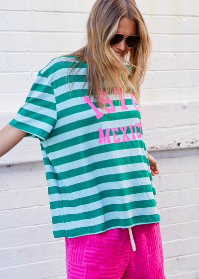 Hammill & Co This tee is a total throwback in the best way. With bold green and light blue stripes and a pop of hot pink “1976 MEXICO” across the front, it’s giving vintage souvenir tee meets cool street style. The fit is oversized and relaxed 