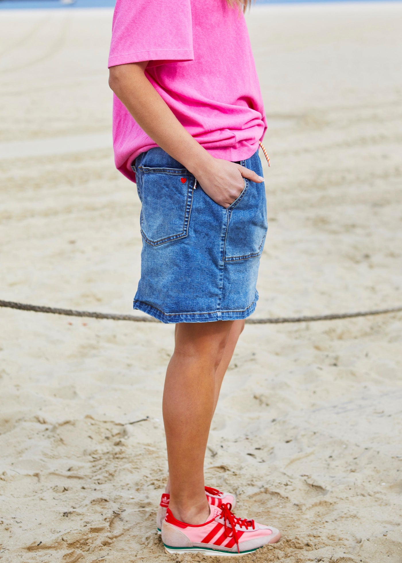 Hammill & Co New stretch denim skirt in slightly distressed stonewash denim. Elastic waist, orange multi draw cord, front scoop pockets, back patch pockets with our red heart embroidery on the back left pocket.