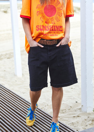 Hammill & Co pair of longer-length black stretch denim shorts with a relaxed fit. They have front pockets, a raw rolled hem, and sit mid-thigh